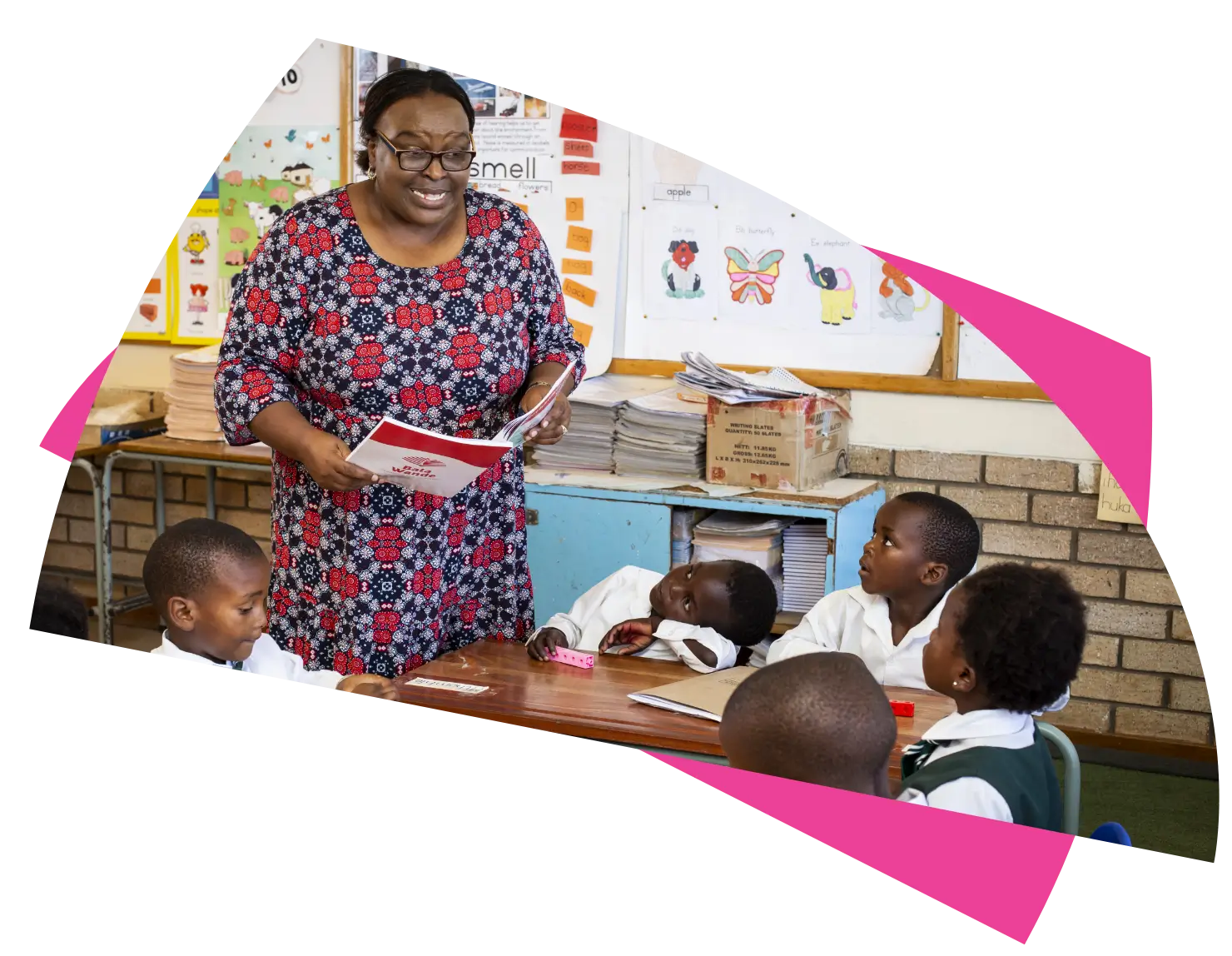 Female teacher holding a text book teaching an attentive group of primary school learners.